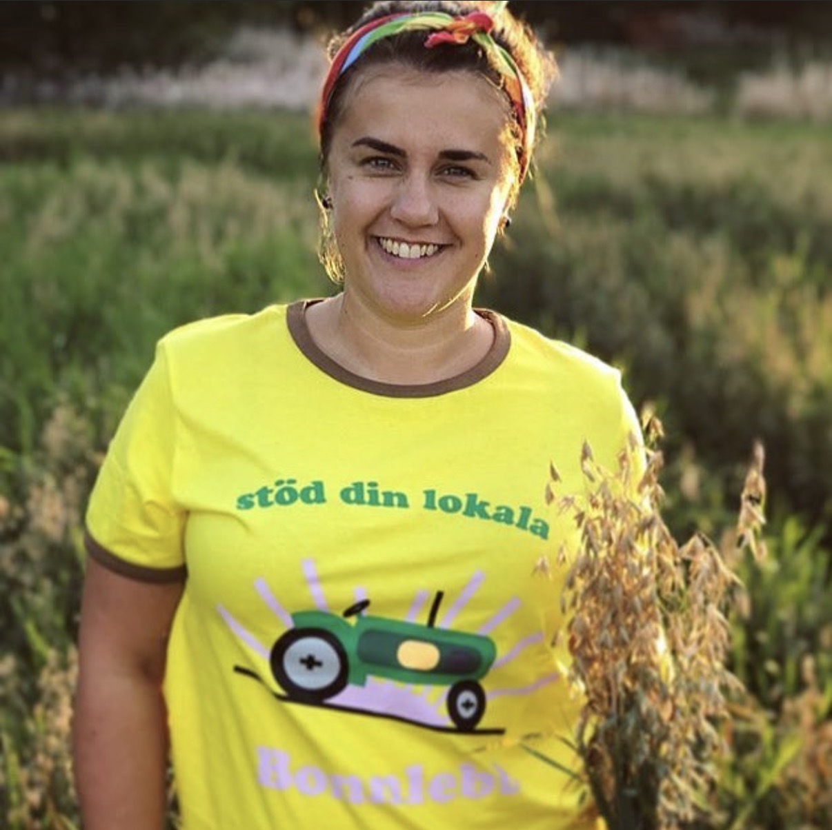 Person i gul t-shirt med traktortryck i ett sädesfält
